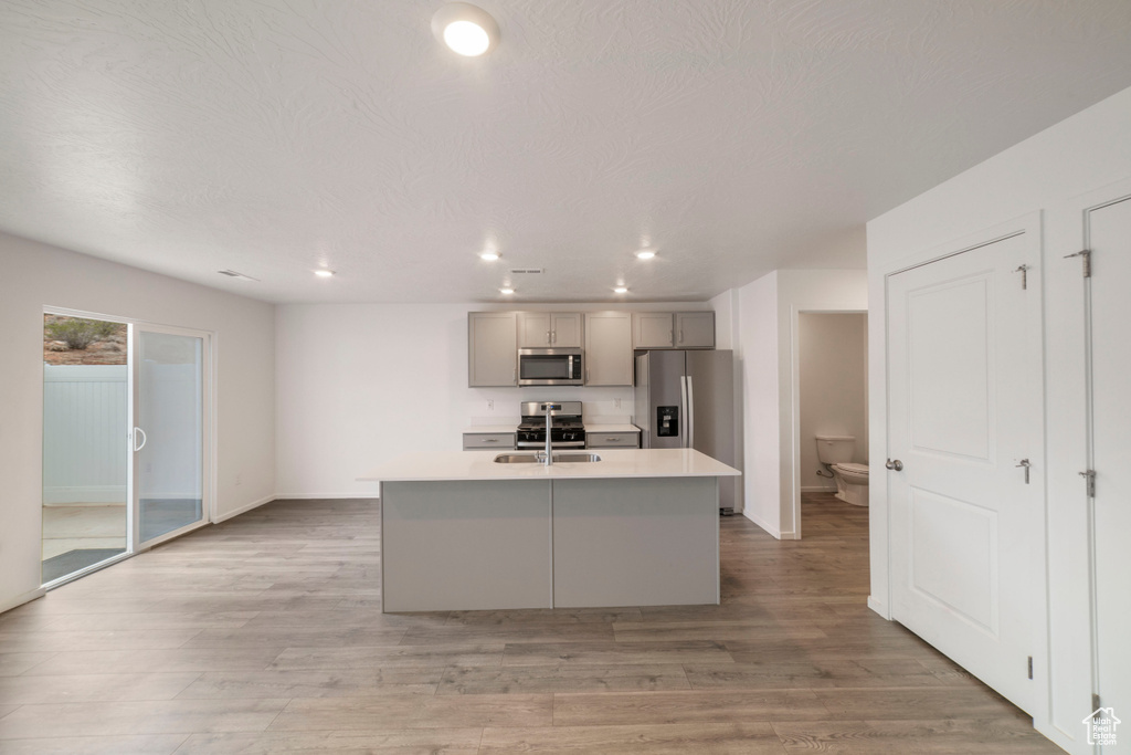 Kitchen featuring appliances with stainless steel finishes, gray cabinets, light countertops, a center island with sink, and recessed lighting