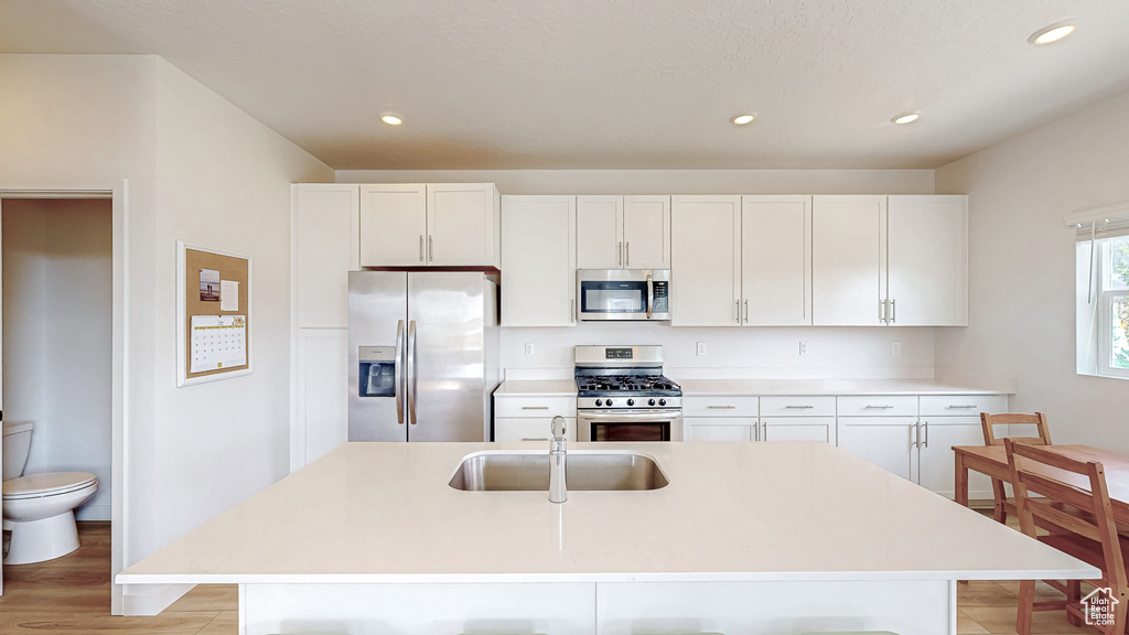 Kitchen with appliances with stainless steel finishes, a sink, recessed lighting, white cabinets, and a kitchen island with sink