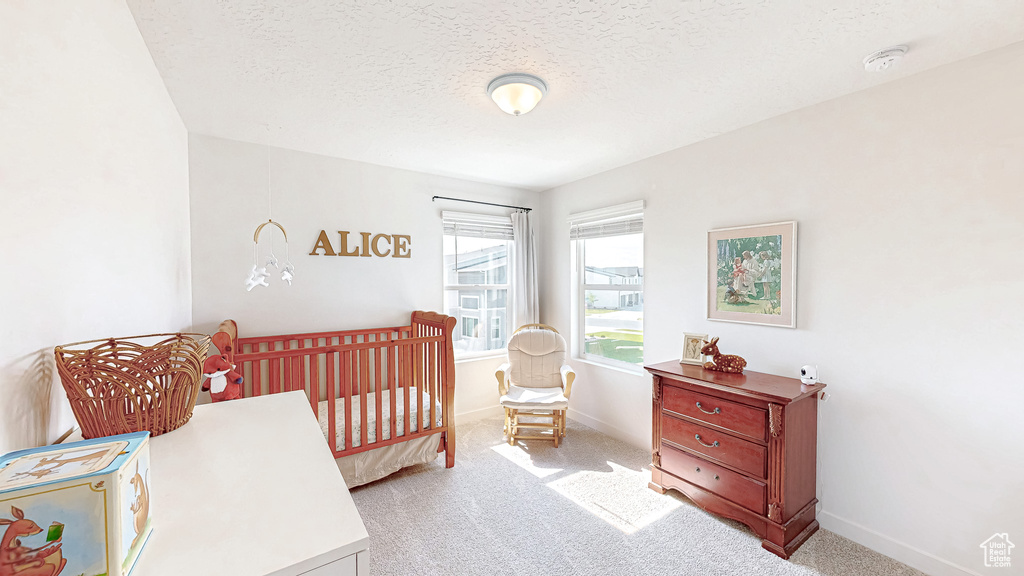Carpeted bedroom with a textured ceiling, baseboards, and a nursery area