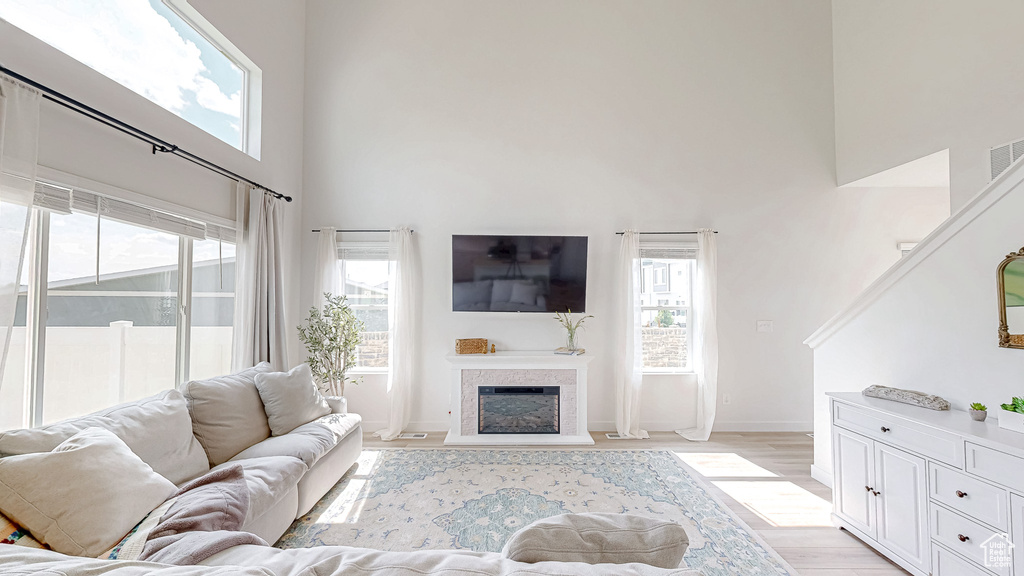 Living area with a high ceiling, healthy amount of natural light, a fireplace, light wood-style flooring, and baseboards