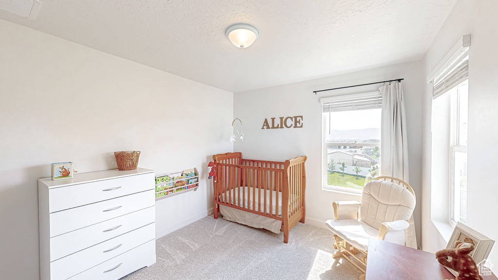 Bedroom with light carpet, a crib, baseboards, and a textured ceiling