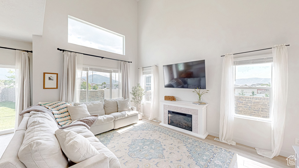 Living room featuring wood finished floors, healthy amount of natural light, a glass covered fireplace, a high ceiling, and baseboards