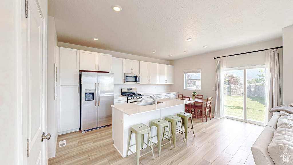 Kitchen with stainless steel appliances, a sink, light wood-style floors, open floor plan, and a kitchen bar
