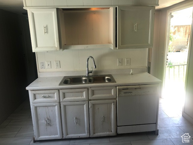 Kitchen featuring white dishwasher, a sink, light countertops, and white cabinets