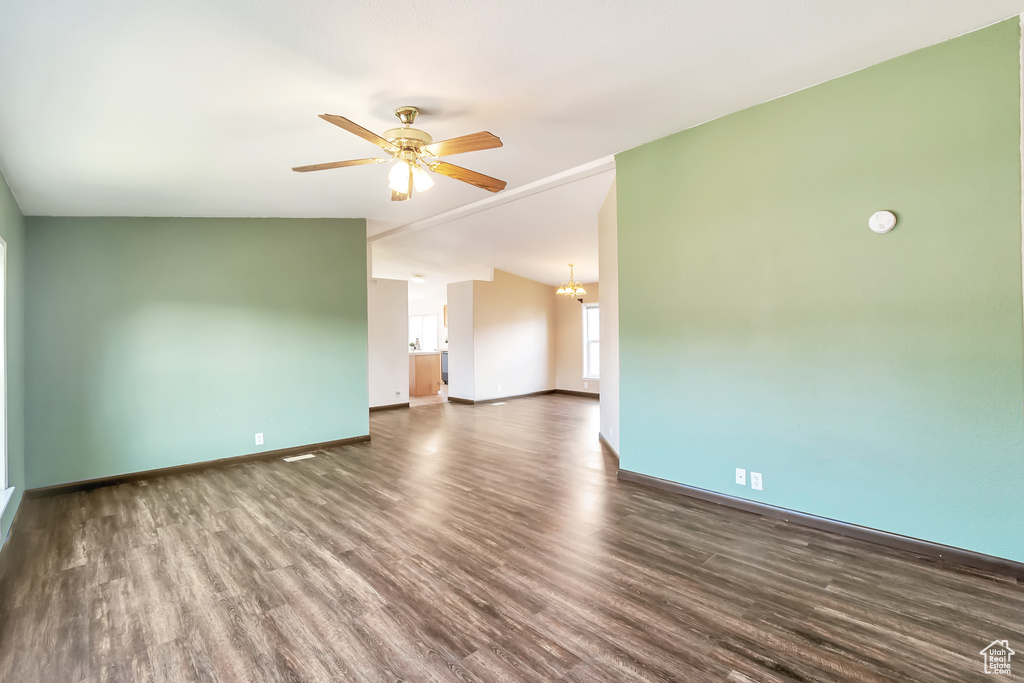 Spare room with wood finished floors, ceiling fan, baseboards, a chandelier, and lofted ceiling