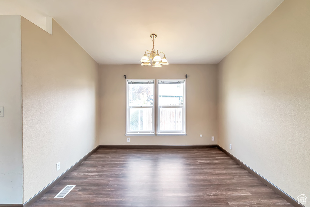 Spare room with a chandelier, wood finished floors, and baseboards