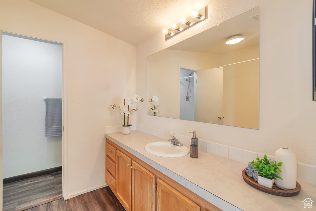 Full bath with wood finished floors, vanity, a shower, and baseboards
