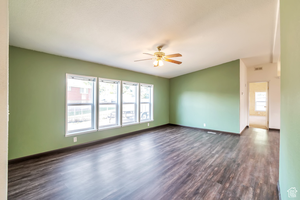 Empty room featuring dark wood-type flooring, ceiling fan, and baseboards