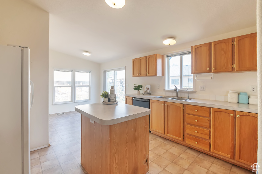 Kitchen with freestanding refrigerator, a sink, lofted ceiling, light countertops, and healthy amount of natural light
