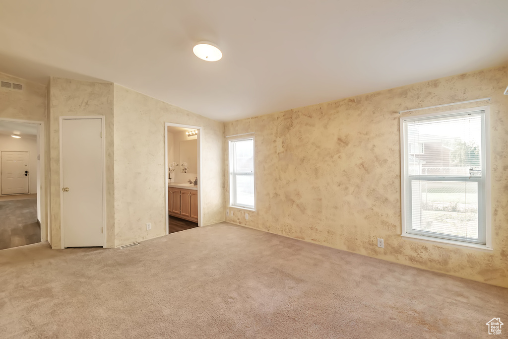 Unfurnished bedroom featuring carpet floors, ensuite bathroom, and vaulted ceiling