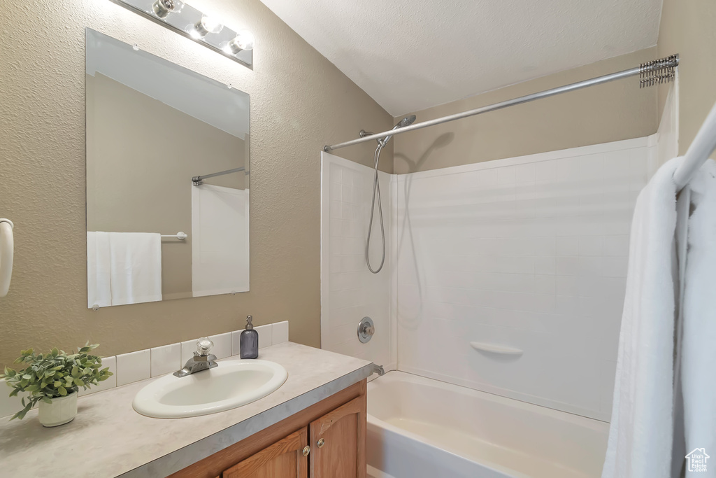 Bathroom with a textured wall, shower / tub combo with curtain, and vanity