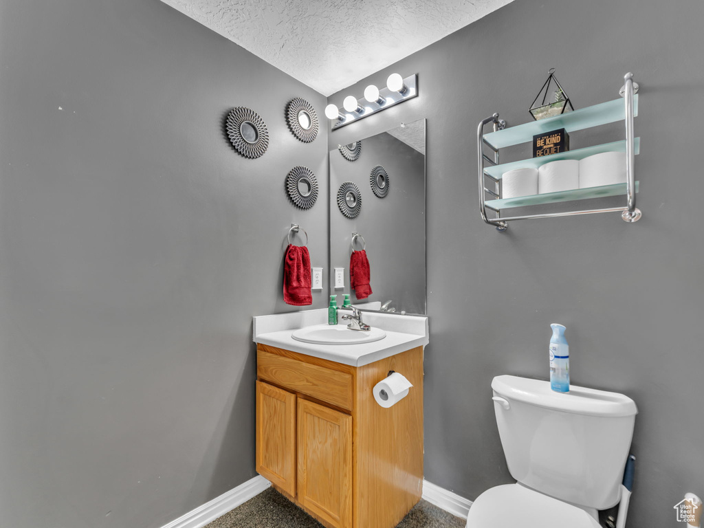 Bathroom featuring vanity, toilet, a textured ceiling, and baseboards