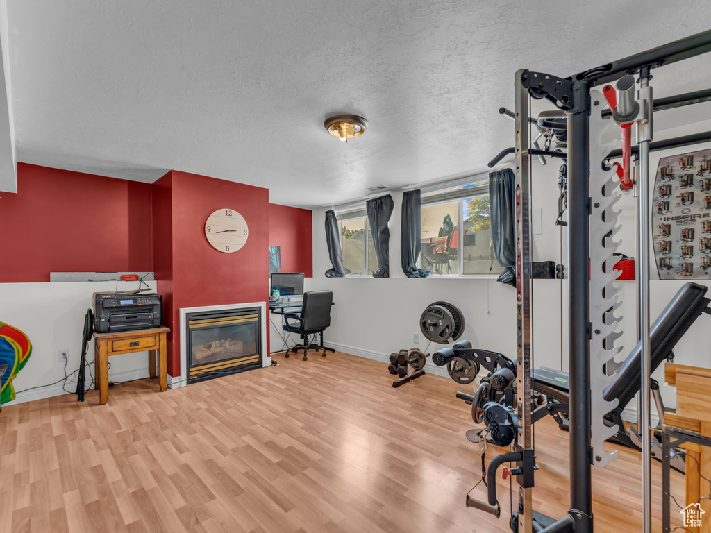 Exercise area featuring baseboards, wood finished floors, a glass covered fireplace, and a textured ceiling