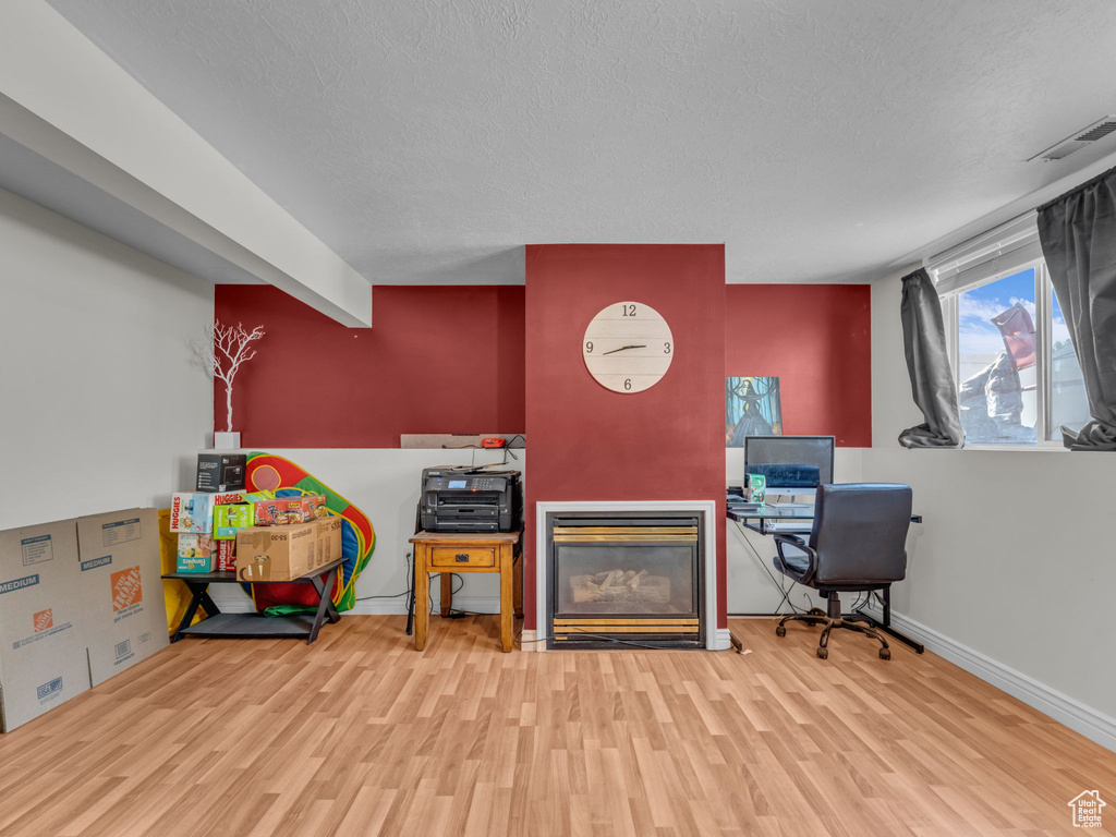 Office space with wood finished floors, a textured ceiling, a glass covered fireplace, and baseboards