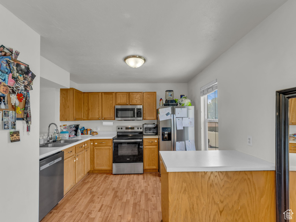 Kitchen featuring stainless steel appliances, a sink, light wood-type flooring, light countertops, and a peninsula