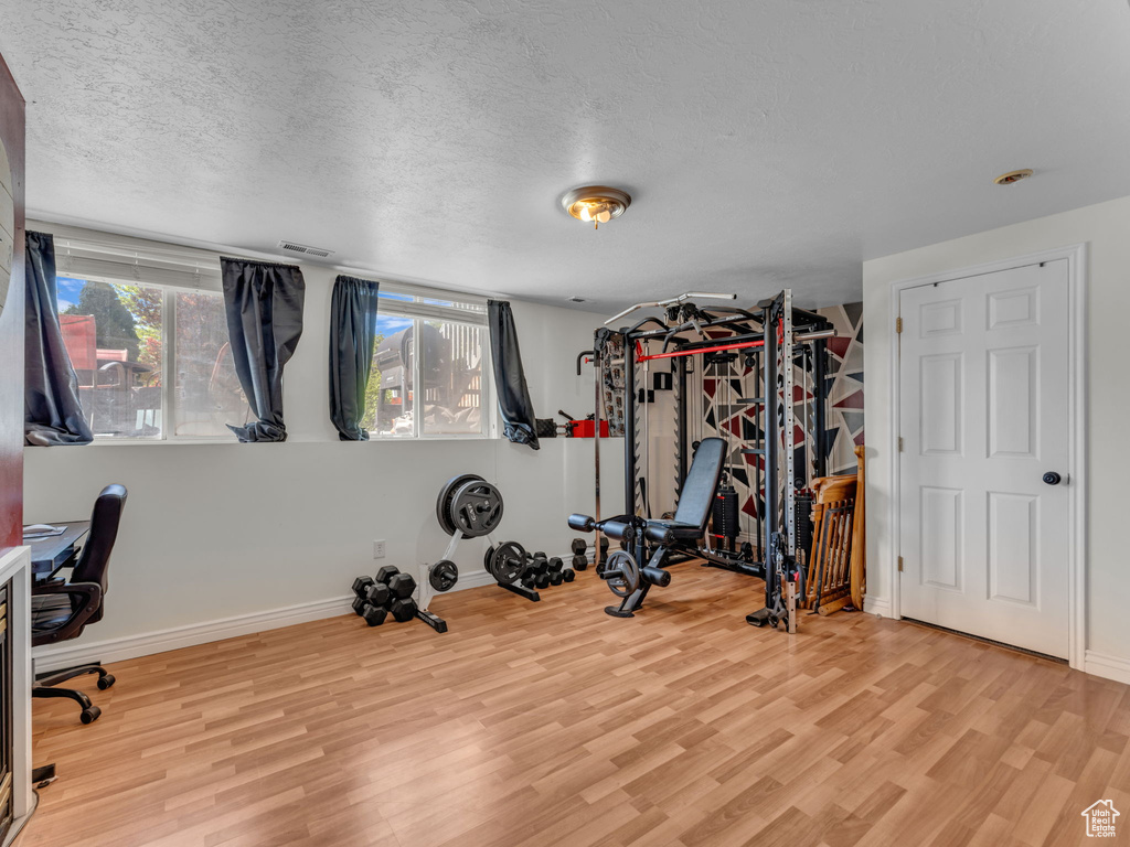 Workout area featuring wood finished floors, healthy amount of natural light, a textured ceiling, and baseboards