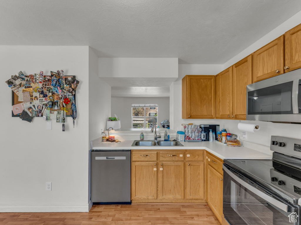 Kitchen with stainless steel appliances, a sink, light countertops, and light wood-type flooring