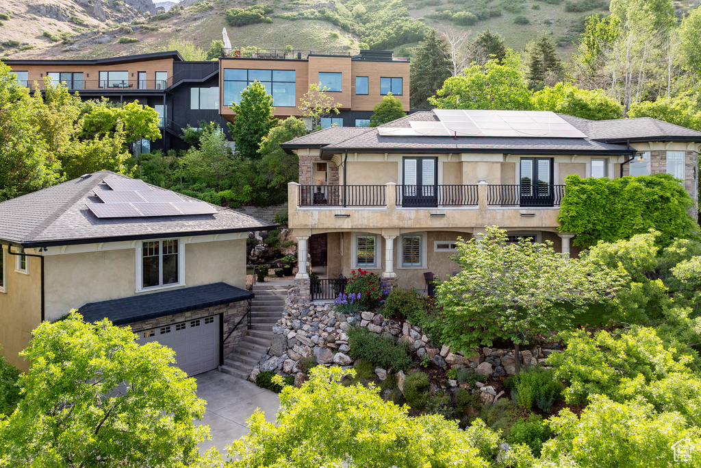 View of front of home featuring a balcony, stucco siding, solar panels, and stairs