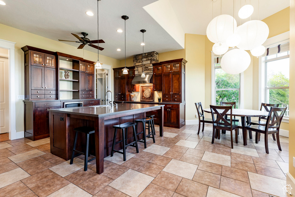 Kitchen with ceiling fan, a sink, open shelves, an island with sink, and dark countertops