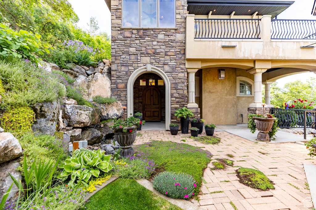 Entrance to property with stucco siding, a balcony, stone siding, and a patio area