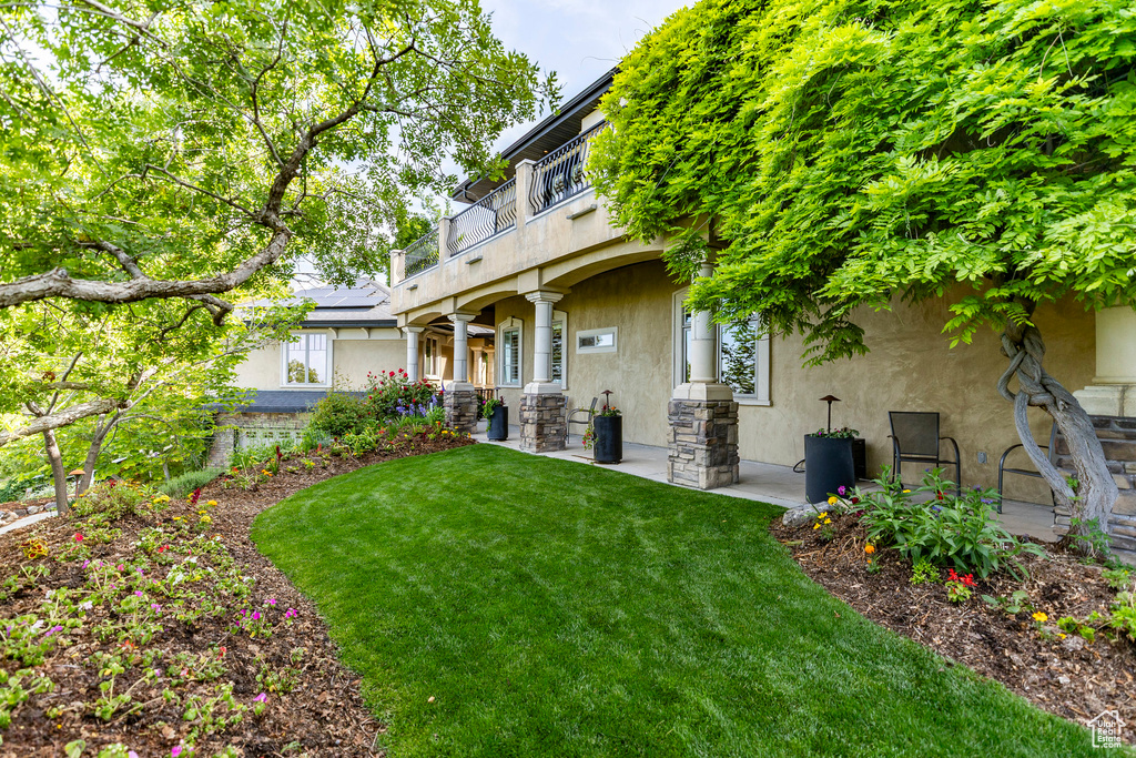 Back of property with stucco siding, a balcony, a lawn, solar panels, and stone siding