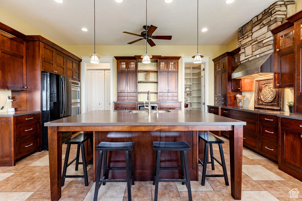 Kitchen with a sink, freestanding refrigerator, ventilation hood, a ceiling fan, and an island with sink