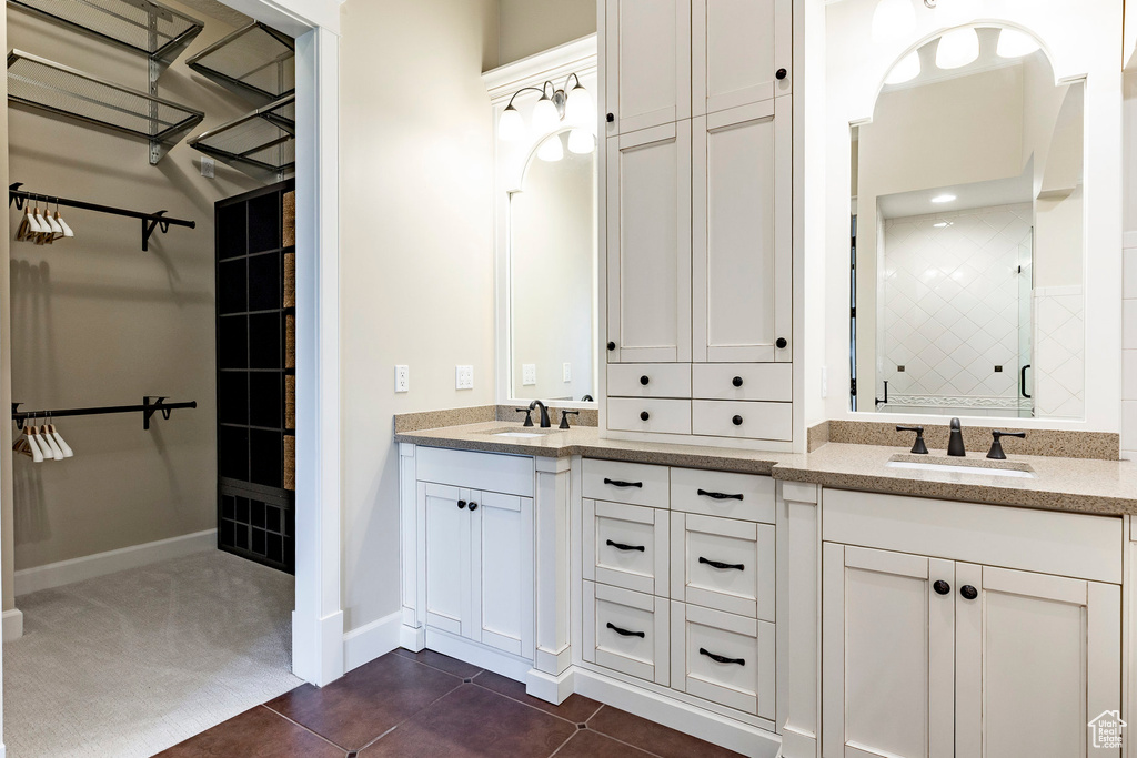 Bathroom featuring double vanity, tile patterned floors, tiled shower, and a walk in closet