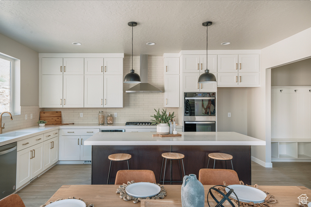Kitchen with wall chimney range hood, appliances with stainless steel finishes, a sink, light wood-style flooring, and white cabinets