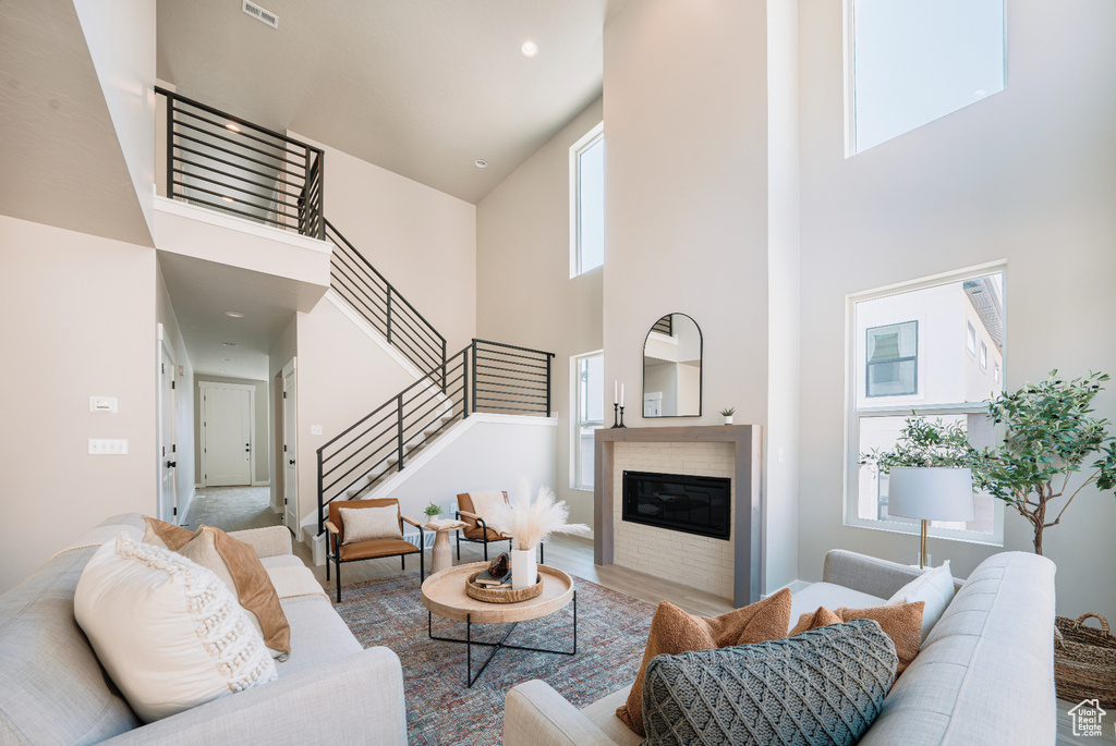 Living area with a high ceiling, stairs, a glass covered fireplace, wood finished floors, and recessed lighting