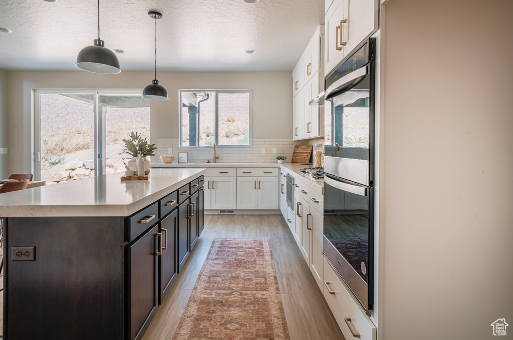 Kitchen featuring white cabinetry, light wood-style floors, a textured ceiling, light countertops, and backsplash