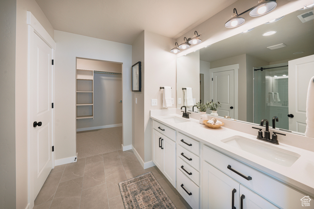 Full bathroom featuring double vanity, a stall shower, a spacious closet, baseboards, and tile patterned flooring