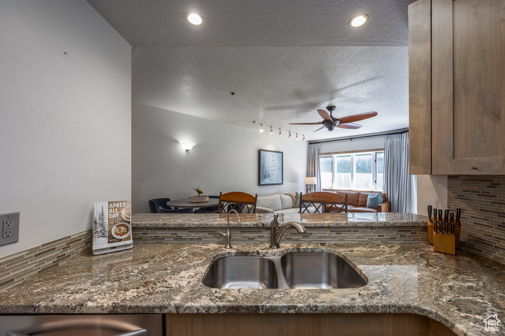 Kitchen with a sink, a textured ceiling, dark stone counters, tasteful backsplash, and ceiling fan