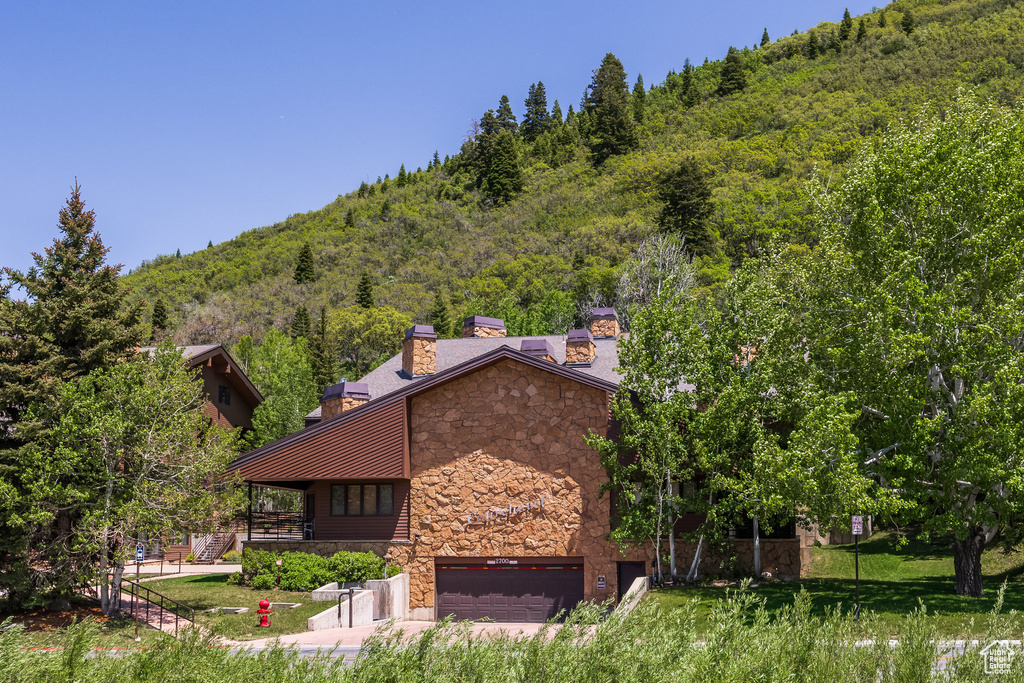 View of side of home with stone siding, a chimney, an attached garage, and a forest view
