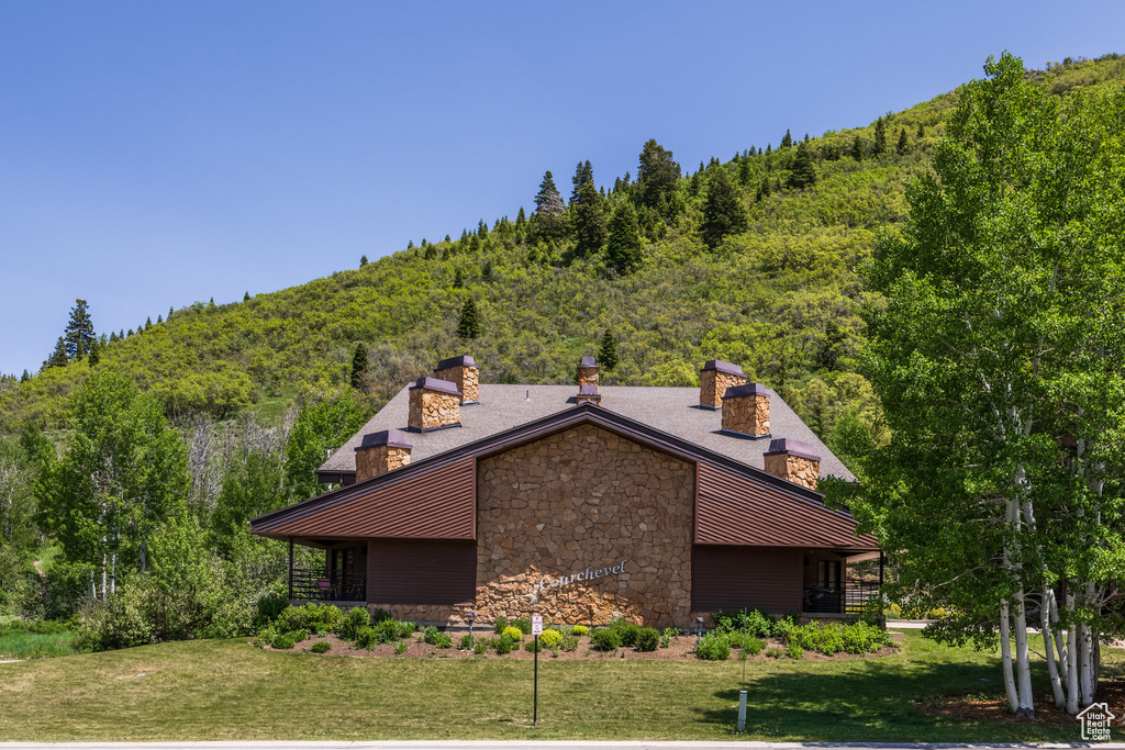 View of property exterior featuring stone siding, a chimney, a standing seam roof, a lawn, and a forest view