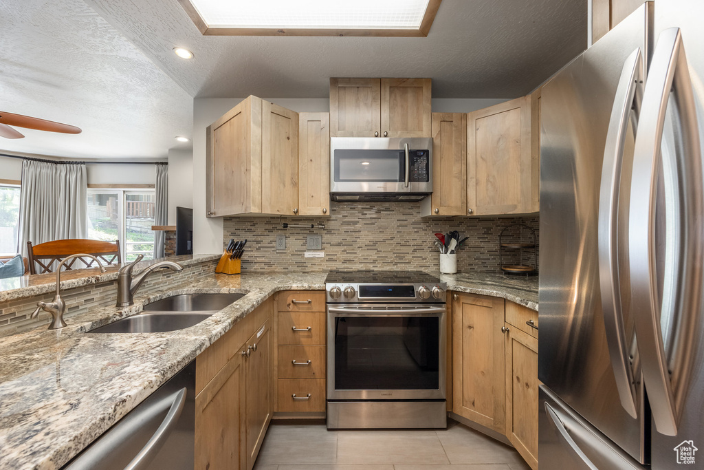 Kitchen featuring stainless steel appliances, a sink, tasteful backsplash, light tile patterned floors, and a ceiling fan