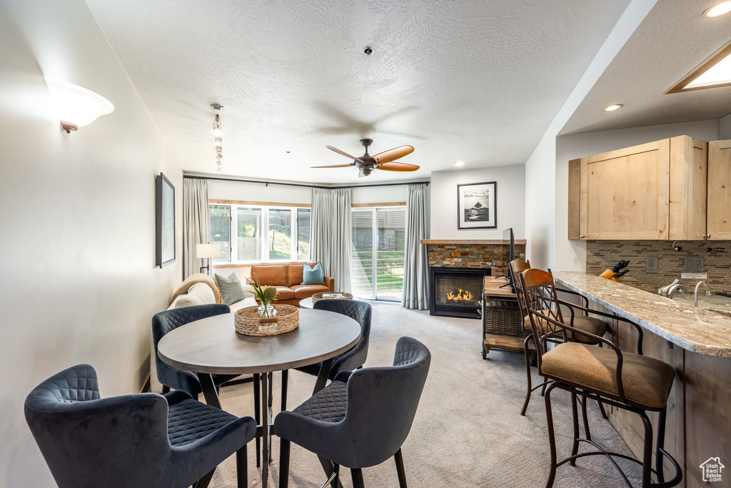 Dining room with light carpet, a textured ceiling, a ceiling fan, a stone fireplace, and recessed lighting