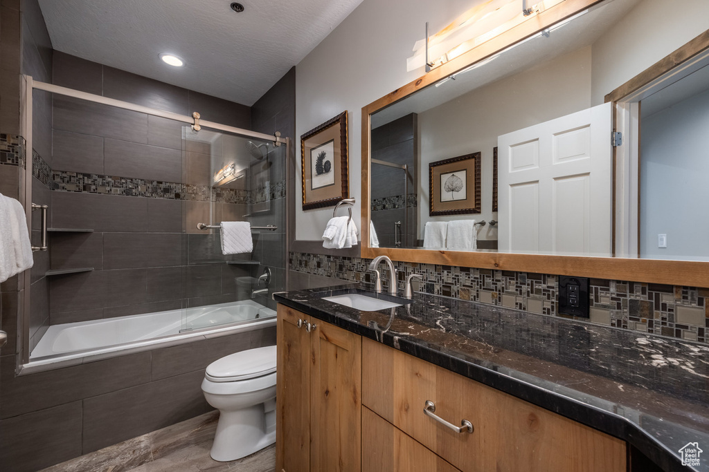 Bathroom with toilet, wood finished floors, tiled shower / bath combo, vanity, and tasteful backsplash