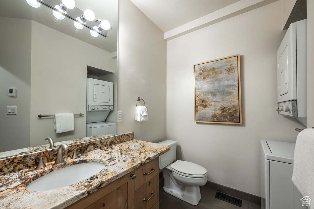 Bathroom with estacked washer and dryer, toilet, vanity, and baseboards