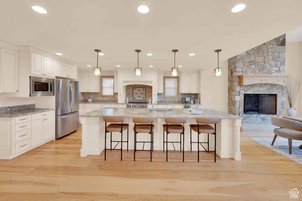 Kitchen featuring appliances with stainless steel finishes, a fireplace, light wood-style flooring, white cabinetry, and recessed lighting