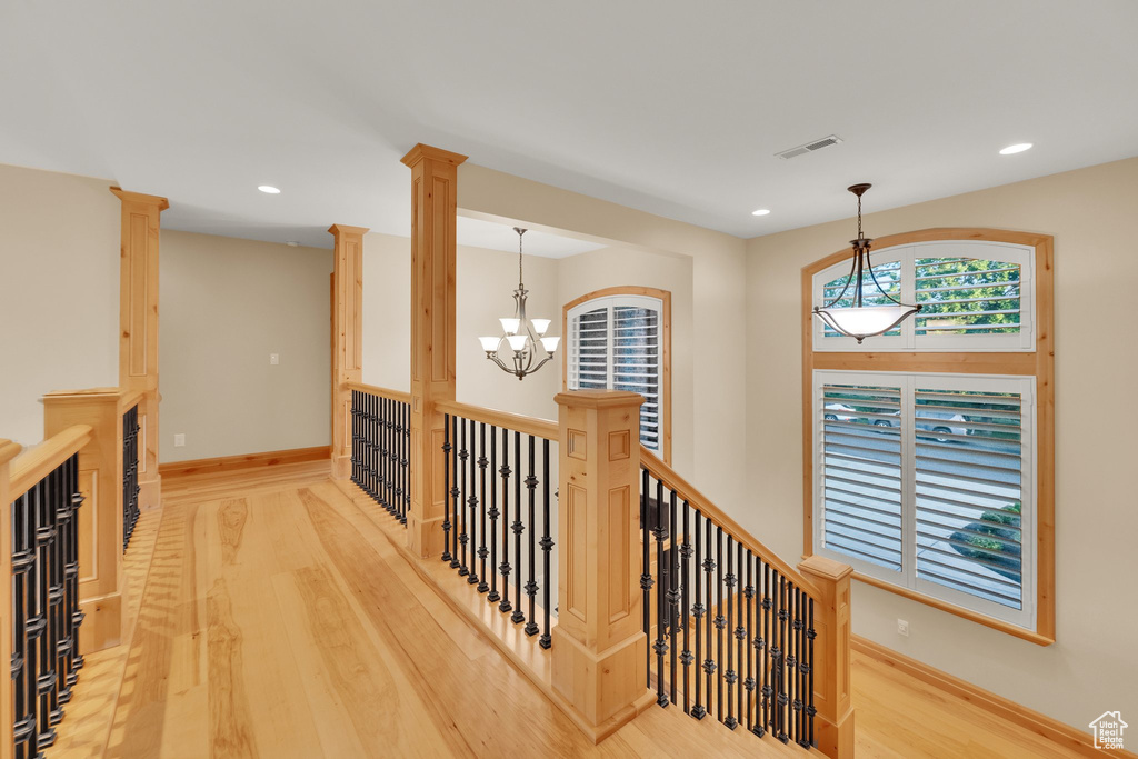 Hall with wood finished floors, a chandelier, recessed lighting, baseboards, and decorative columns