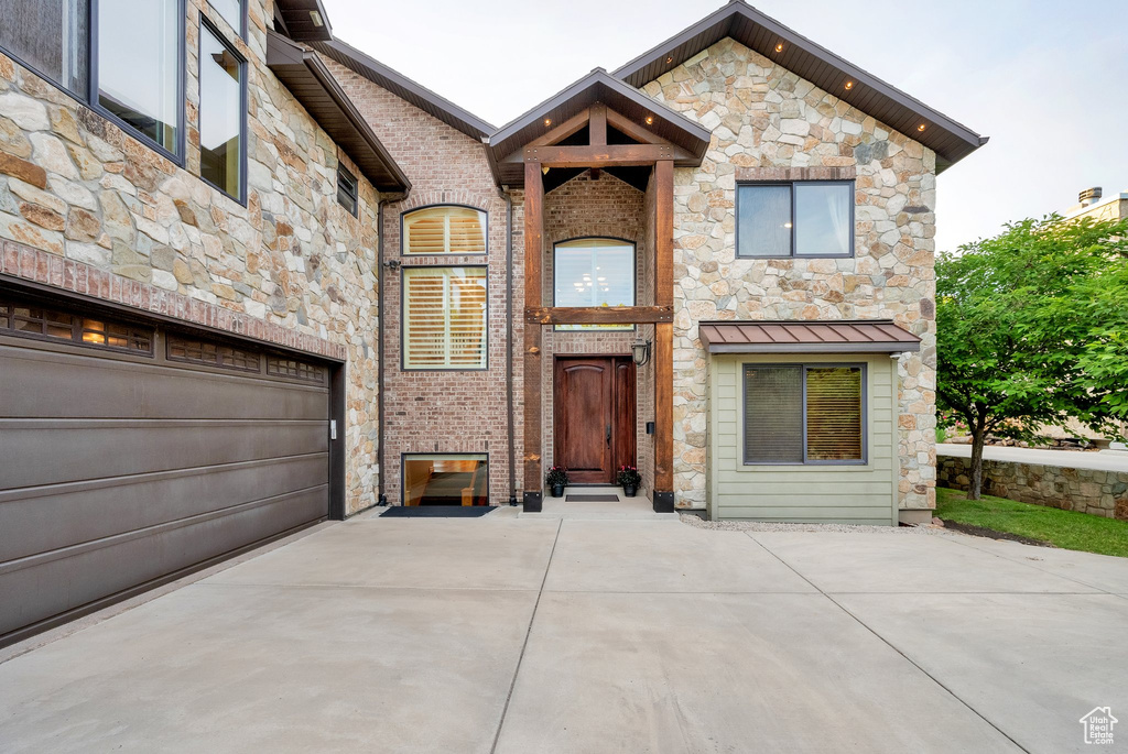 View of front of property with stone siding, concrete driveway, a garage, and a standing seam roof