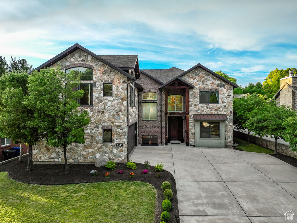 French country inspired facade with stone siding, a front yard, and driveway