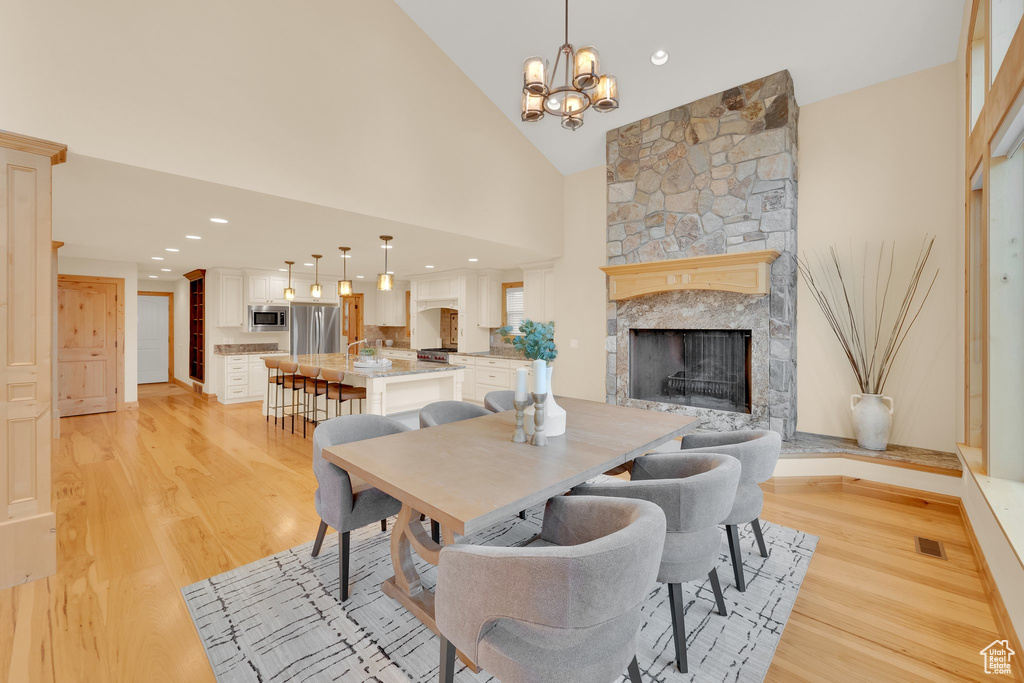 Dining room featuring a stone fireplace, light wood-style flooring, high vaulted ceiling, a chandelier, and recessed lighting