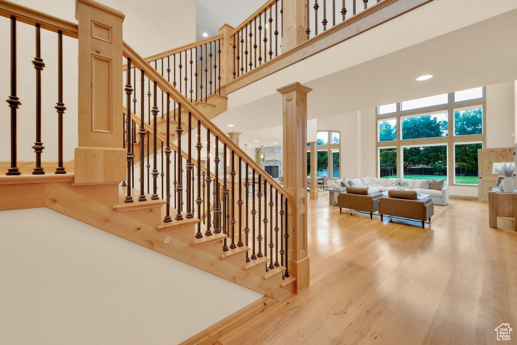 Stairway featuring a towering ceiling, wood finished floors, recessed lighting, and decorative columns