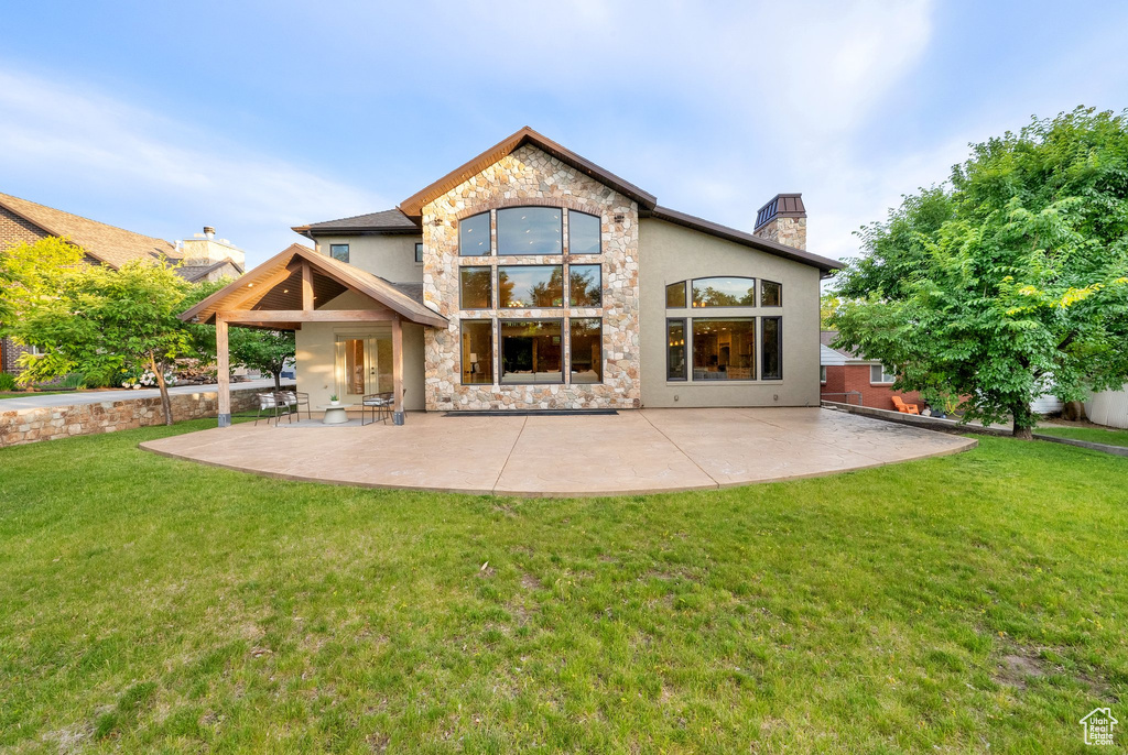 Back of property with stone siding, stucco siding, a chimney, and a patio