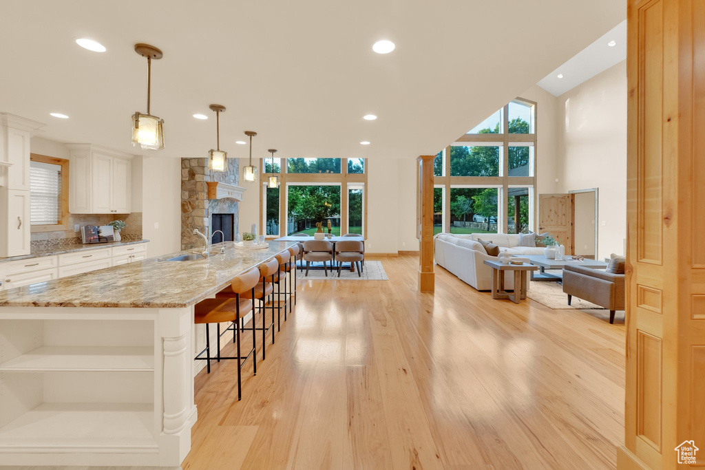 Kitchen featuring a sink, light wood finished floors, light stone counters, a stone fireplace, and white cabinetry