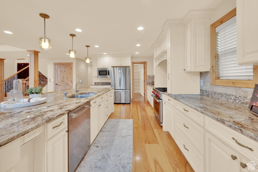 Kitchen featuring stainless steel appliances, a sink, light wood finished floors, hanging light fixtures, and tasteful backsplash