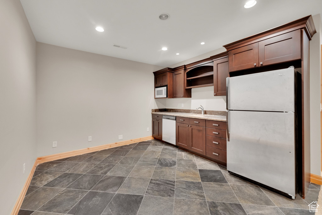 Kitchen featuring white appliances, a sink, open shelves, stone finish floors, and baseboards