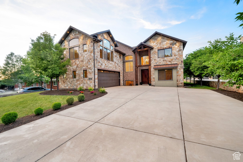 View of front of home featuring stone siding, an attached garage, concrete driveway, and a front yard