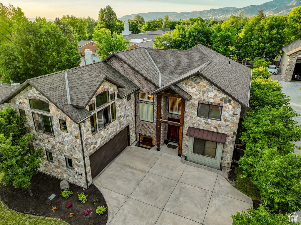 View of front of home with stone siding, driveway, an attached garage, and a shingled roof